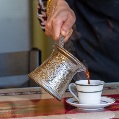 Traditional coffee is being poured from a pot into a small cup.