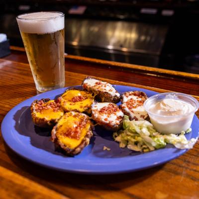 Plate of loaded potato skins served with a dipping sauce and a tall glass of beer.