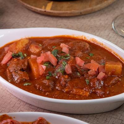 A rich, red lamb curry with diced potatoes and fresh tomato garnish.