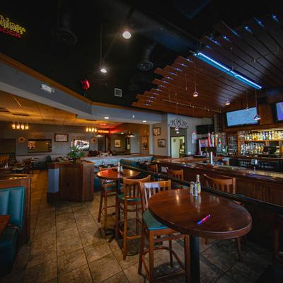 Restaurant interior with wooden tables, teal cushioned booths, and a dimly lit bar..