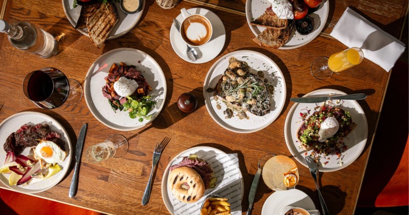 An overhead view of a wooden table filled with diverse brunch dishes and drinks