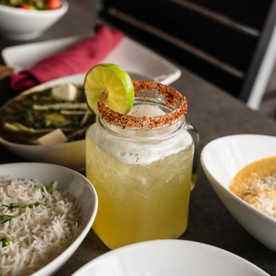 A cocktail served in a mason jar, accompanied by several food dishes..