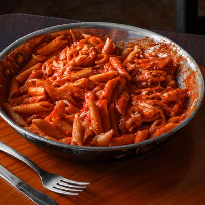 Plate of pasta in tomato sauce, served on the table with cutlery.