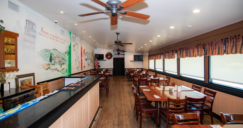 Interior of a restaurant with a mural, bar counter, several wooden tables, and large windows