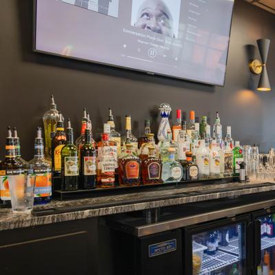 Assorted liquor bottles neatly arranged on a bar shelf underneath a TV.