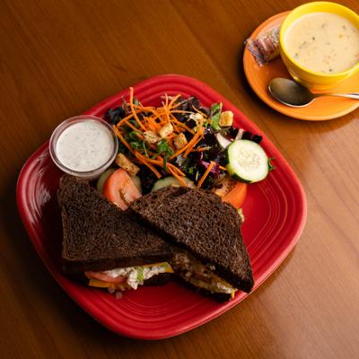 Chicken Salad Sandwich on dark ry served with a side salad and a small cup with sauce.