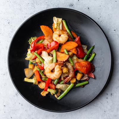 Stir-fried shrimp and mixed vegetables on a black plate.