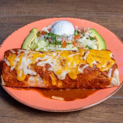 Carnitas Burrito topped with sauce and melted cheese, served with a salad and sour creme.
