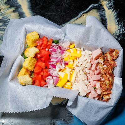 Club salad with ingredients arranged in rows within a lined box.