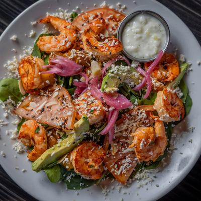 Shrimp salad with spinach, avocado, cheese, pickled red onions, and dressing on the side.