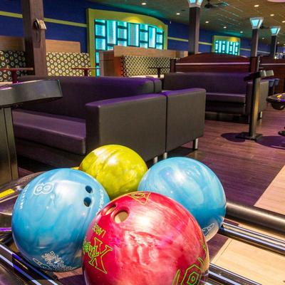 Four colorful bowling balls rest on a rack inside a bowling alley.