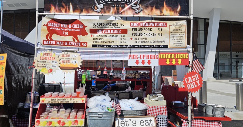 Outdoor BBQ stall selling sandwiches, mac and cheese, and lemonade