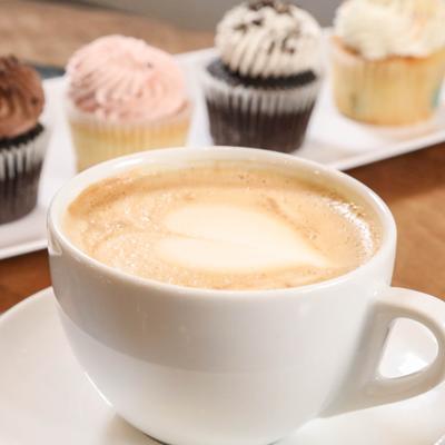 A cup of latter sits on a table with assorted cupcakes in the background.