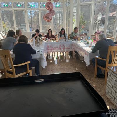 A group of people dining at a table in a sunlit glasshouse with balloons.