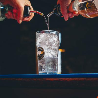 Hands pouring drinks together into a single glass.