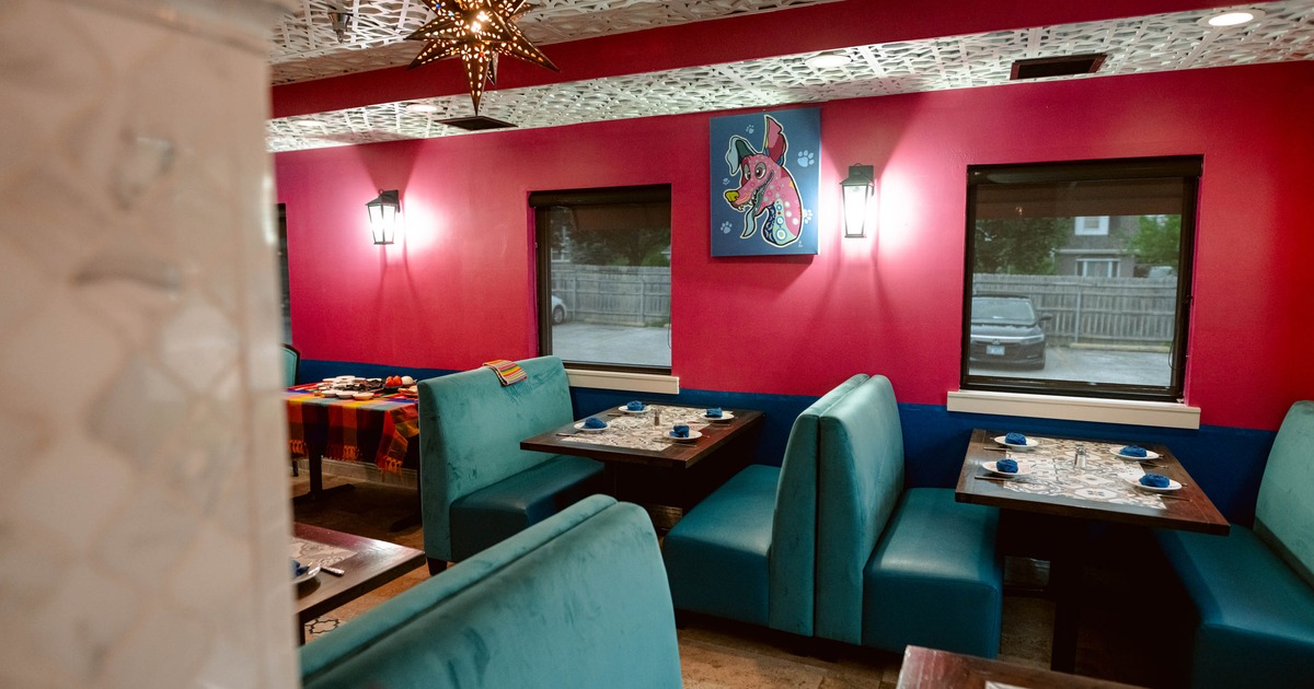 Interior of a restaurant with pink walls, teal booths, a patterned ceiling, and a colorful elephant painting