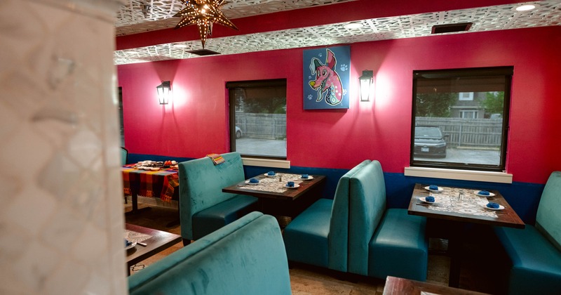 Interior of a restaurant with pink walls, teal booths, a patterned ceiling, and a colorful elephant painting