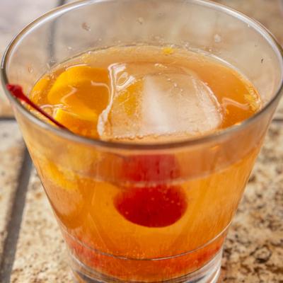 Old Fashioned cocktail with lemon peel and a cherry on a stone tabletop.