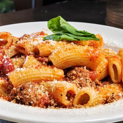 Rigatoni pasta with tomato meat sauce, grated cheese and basil in a white bowl..