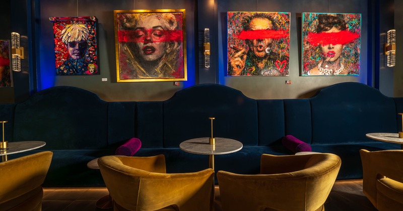 Interior, paintings, dark blue seating, marble tables, and mustard yellow armchairs