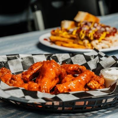 Buffalo wings in a basket near a plate of loaded fries dish.
