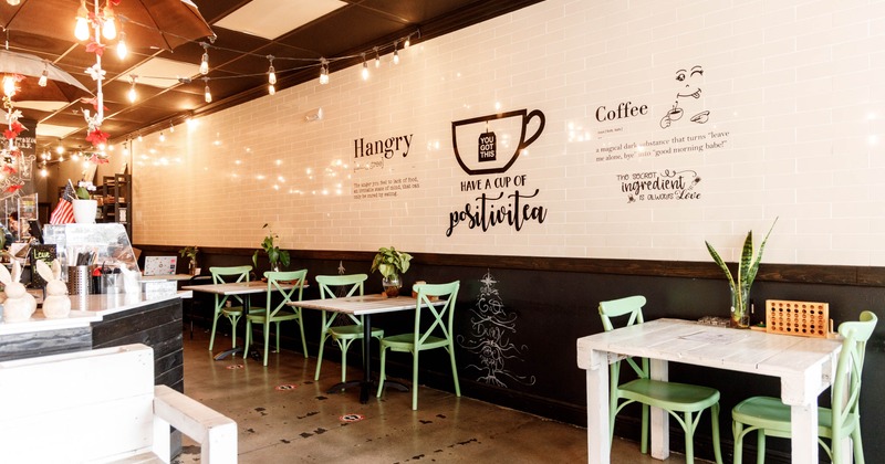 Interior of a café with white tiled walls, green chairs, wooden tables