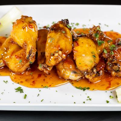Chicken wings glazed in a sweet chili sauce, garnished with fresh herbs.