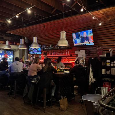 Bar area with people seated at the counter, overhead lightinig and television screens.