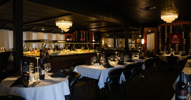 Elegant interior - white-tablecloth tables, a buffet, chandeliers & walls lined with wine bottles.