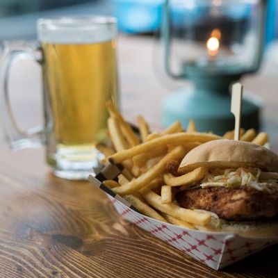 Close-up of a chicken slider with fries and a beer in the background.