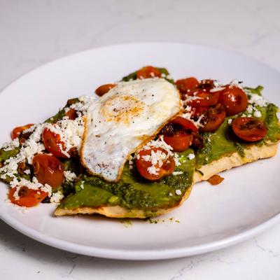 Avocado toast, topped with cherry tomatoes, cheese, and fried egg.