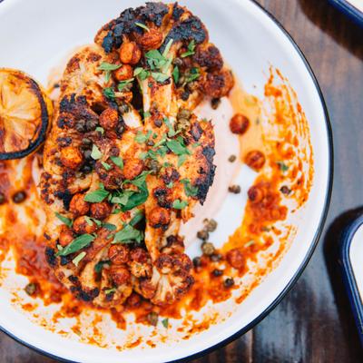Charred cauliflower steak, with hot chili sauce, yogurt, capers, chickpeas, and charred lemon.