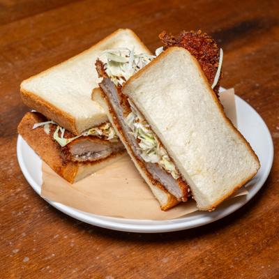 Katsu sando sandwich with breaded cutlet and slaw on a white plate.