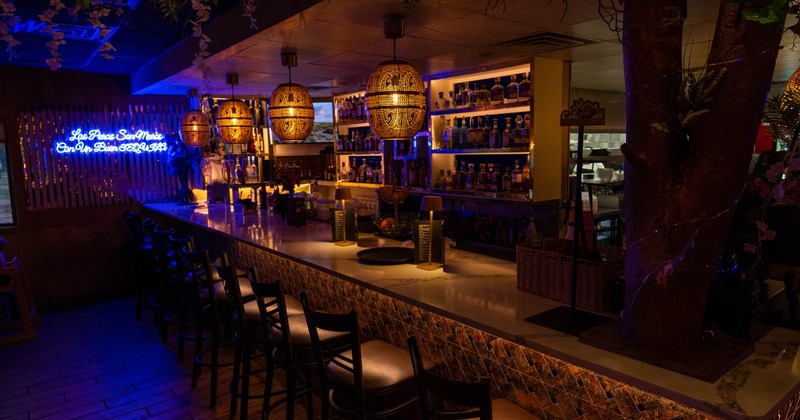 Dimly lit bar with a long counter, bar stools, and hanging woven pendant lights