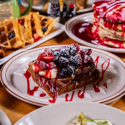 French toast topped with berries and sauce, pancakes and waffles in the background.
