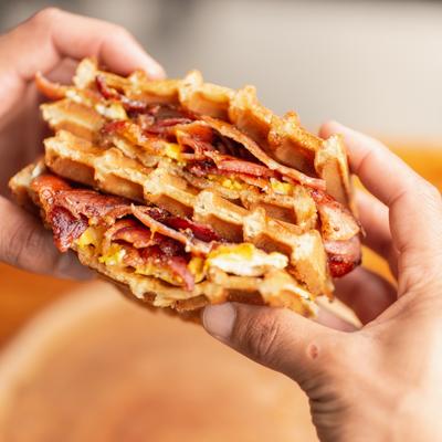Hands holding a waffle sandwich.
