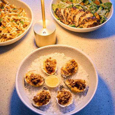 Oysters on crushed ice with topping and lemon beside candlelit dishes.