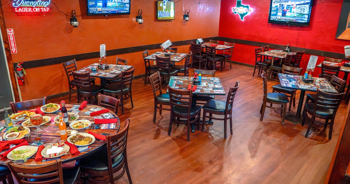Interior of a restaurant with tables and chairs, TV screens, and neon signs on the walls