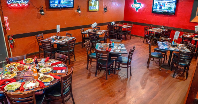 Interior of a restaurant with tables and chairs, TV screens, and neon signs on the walls