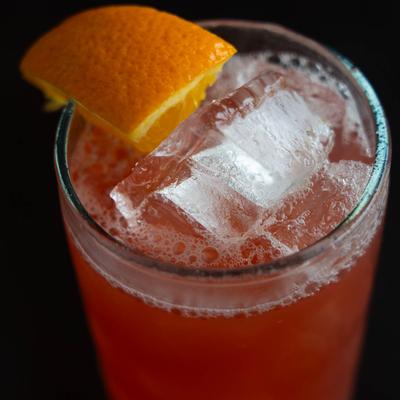 Close up of Ruby Relaxer cocktail with a fresh orange slice perched on the rim.