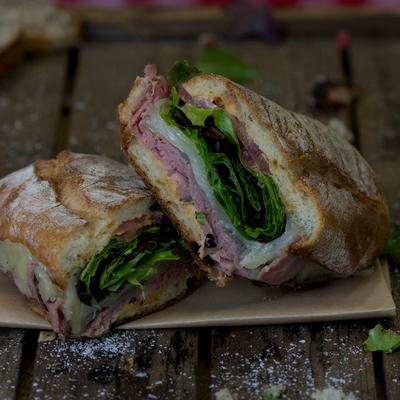 Sandwich featuring a crusty bread filled with layers of meats, cheese and greens.