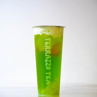 A tall, translucent cup filled with vibrant green tea topped with foam.