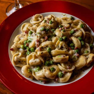 Creamy tortellini pasta with peas on a red plate.