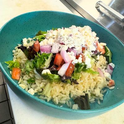 Greek-style rice bowl topped with fresh salad and feta cheese.