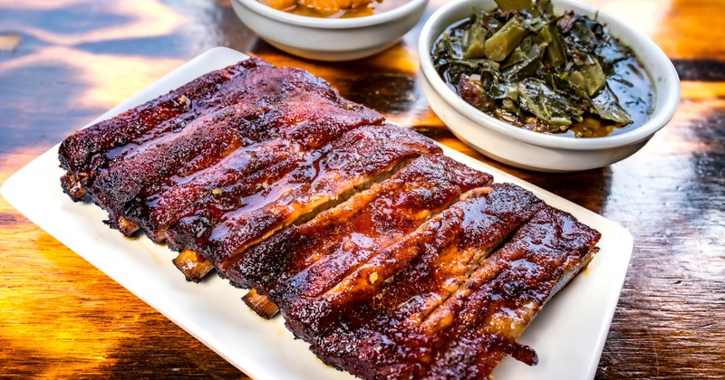 Rack of BBQ ribs served with sides of collard greens and yams