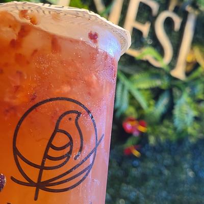 Strawberry iced tea in a clear cup with a logo.