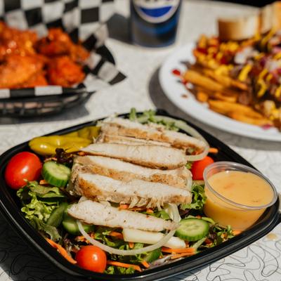 Grilled chicken salad served with creamy dressing, accompanied by other dishes.