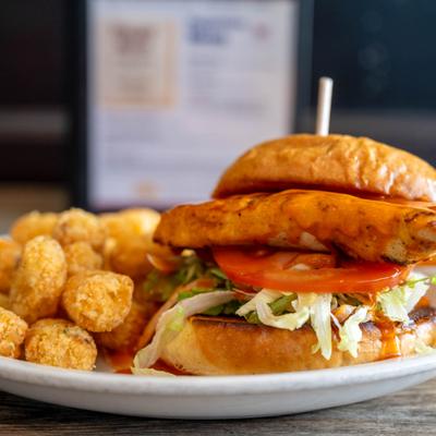 Acadian Chicken Sandwich with avocado, lettuce, tomato, and a side of tater tots.
