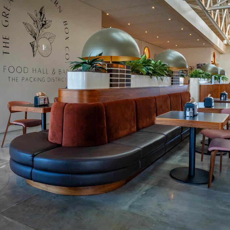 Modern food hall with brown and red seating, green plants, and dome pendant lights