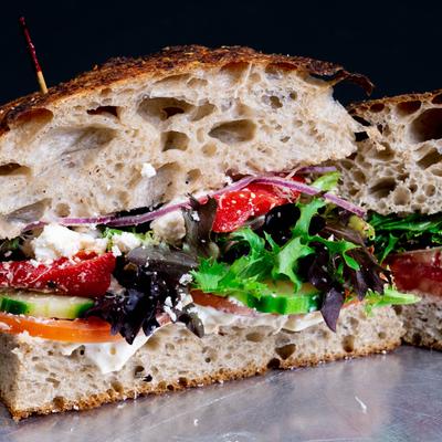Veggie focaccia sandwich with greens, tomato, and feta cheese.